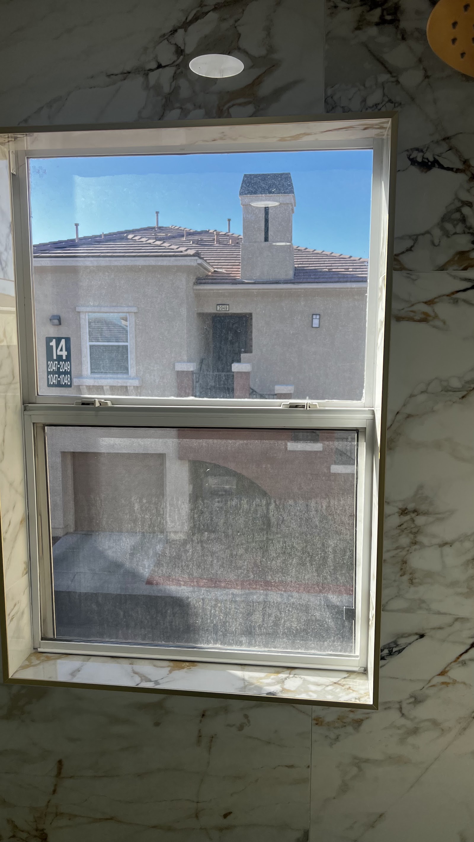 Tinted residential double-hung window in a marble-tiled room